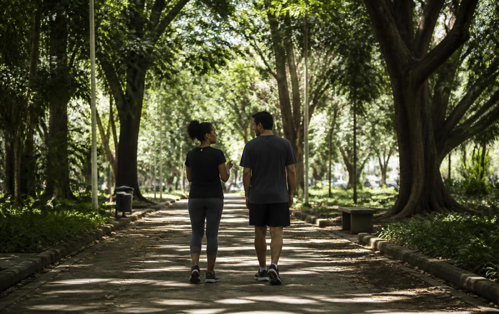 Duas pessoas caminhando e conversando em uma trilha arborizada de parque urbano